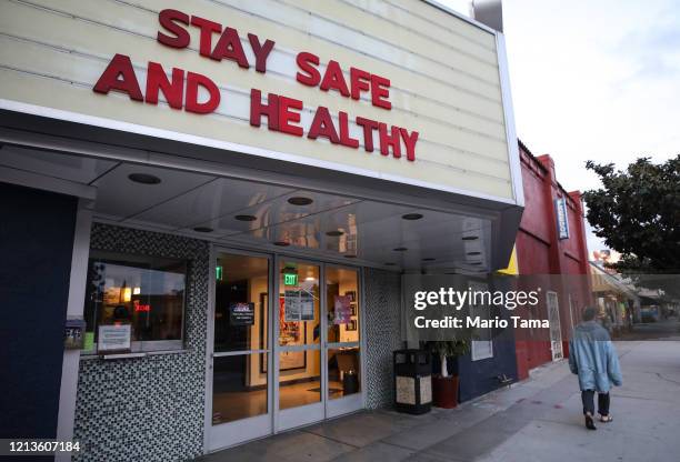 Pedestrian walks past a shuttered movie theater, with the message 'Stay Safe and Healthy' displayed on the marquee, on March 19, 2020 in Los Angeles,...