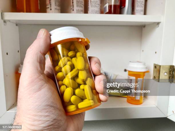 man's hand holding bottle of prescription medication with medicine cabinet in background - armoire de toilette photos et images de collection