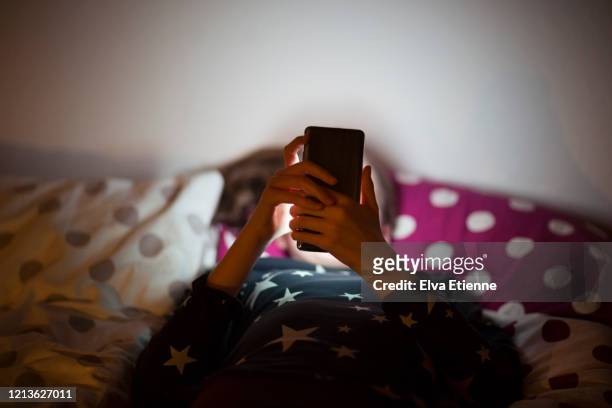 girl lying on bed at night and using a mobile phone - cara oculta fotografías e imágenes de stock