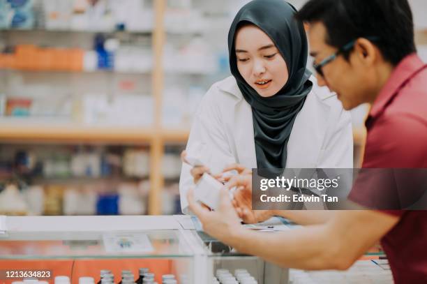 an asian malay female pharmacist with hijab is explaining to her customer on the prescription medicine at the counter - pharmacist and patient stock pictures, royalty-free photos & images