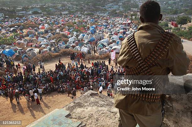 Militiaman watches as people wait for cooked food at camp for Somalis displaced by drought and famine on August 18, 2011 in Mogadishu, Somalia. The...