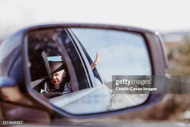 car mirror shot of boy in back seat with hand out window on sunny day - rear view mirror stock pictures, royalty-free photos & images