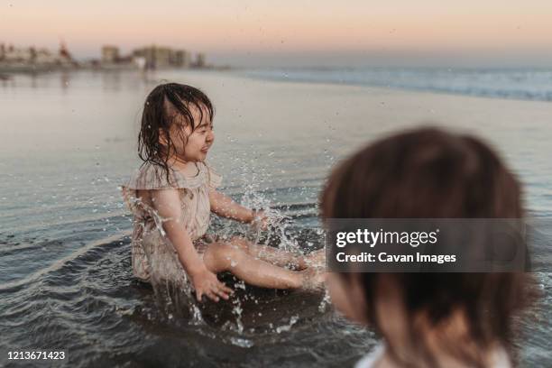 happy 2 year old girl splashing in water at beach - bathing in sunset stockfoto's en -beelden