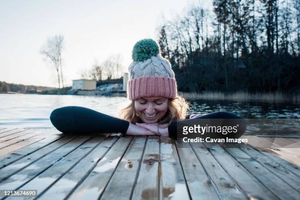 woman smiling leaning on a jetty whilst in the sea cold water swimming - cold woman stockfoto's en -beelden