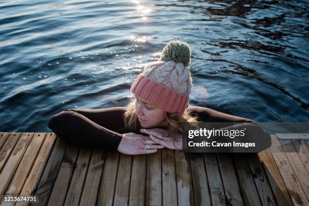 woman leaning on a pier whilst in the water cold water swimming - eis baden stock-fotos und bilder