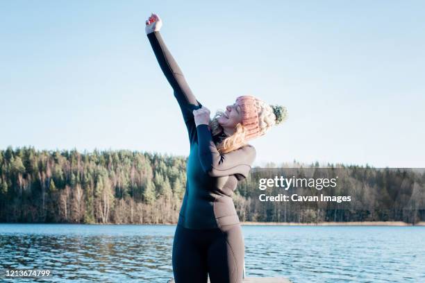 woman putting a wetsuit on for cold water swimming at the beach - eis baden stock-fotos und bilder