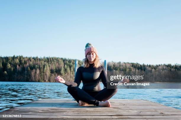 woman meditating in a wetsuit at the beach before cold water swimming - yoga in the snow stock-fotos und bilder