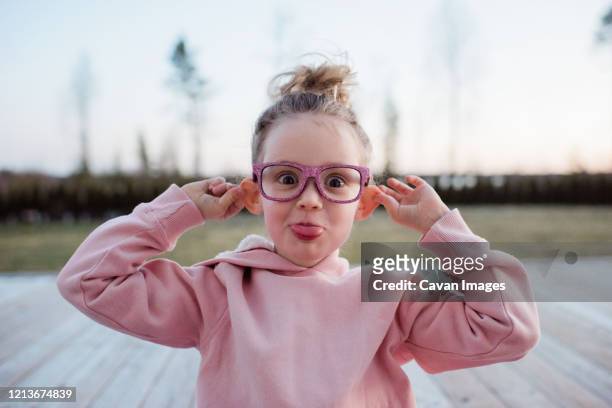 portrait of a young girl pulling silly faces with pink sparkly glasses - funny facial expression stock pictures, royalty-free photos & images