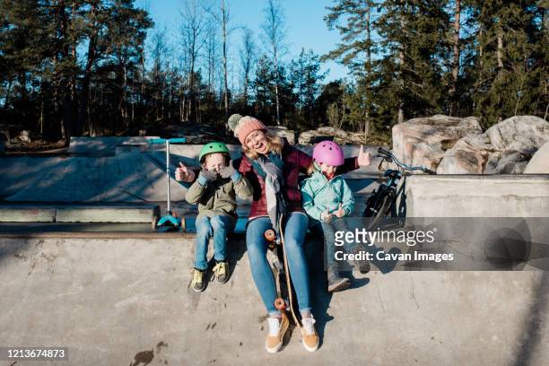 mom and her kids playing at a skate park with scooters and bikes - mother and daughter riding on skateboard in park stock pictures, royalty-free photos & images