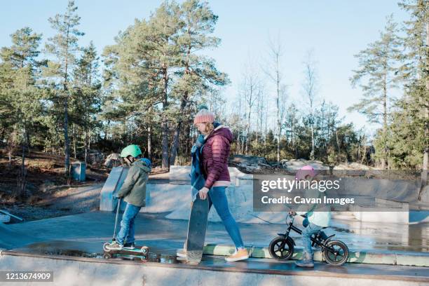 mom and her kids walking across a skatepark to ride and have fun - mother and daughter riding on skateboard in park stock pictures, royalty-free photos & images