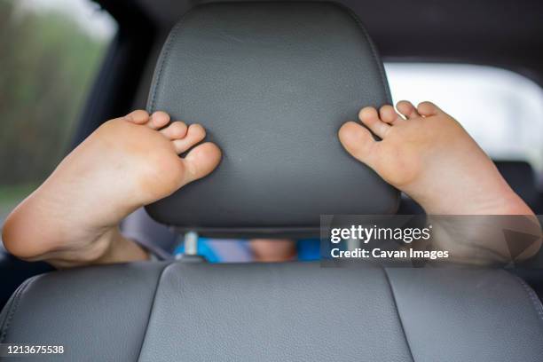 a child in the backseat of a car wraps his feet round the front seat - repose tête photos et images de collection