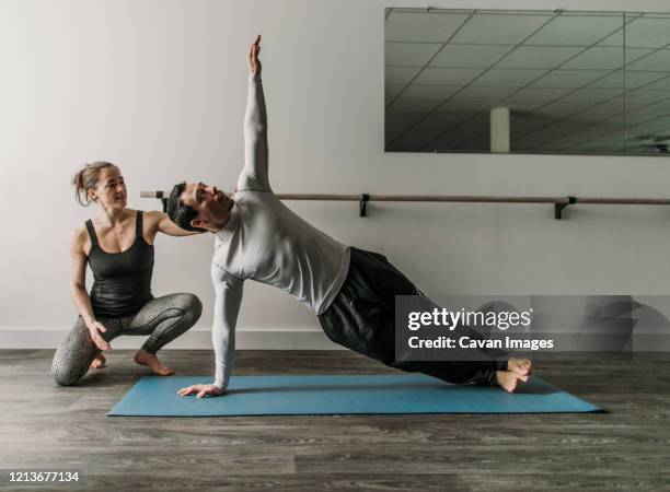 female personal trainer coaches male client doing a sideways plank - metodo pilates foto e immagini stock