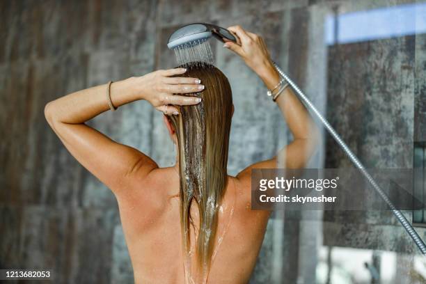 vista trasera de una mujer lavándose el pelo debajo de la ducha. - lavarse el cabello fotografías e imágenes de stock