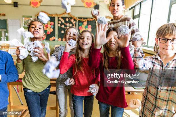rude school children throwing crumpled papers on a teacher in the classroom. - naughty kids in classroom stock pictures, royalty-free photos & images
