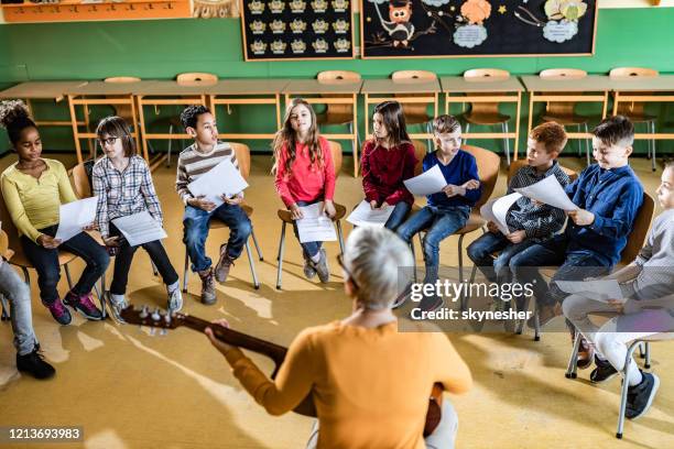 grote groep basisstudenten die een muziekklasse met hun leraar hebben. - african childrens choir stockfoto's en -beelden