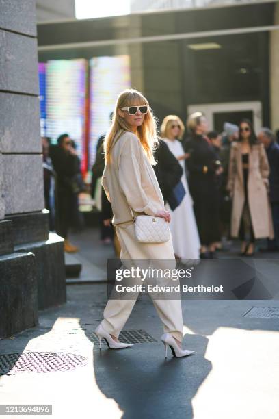 Jeanette Madsen wears sunglasses, earrings, a Balenciaga cream-color sweater, cream-color wide-legs pants, a white quilted bag, white pointy heeled...