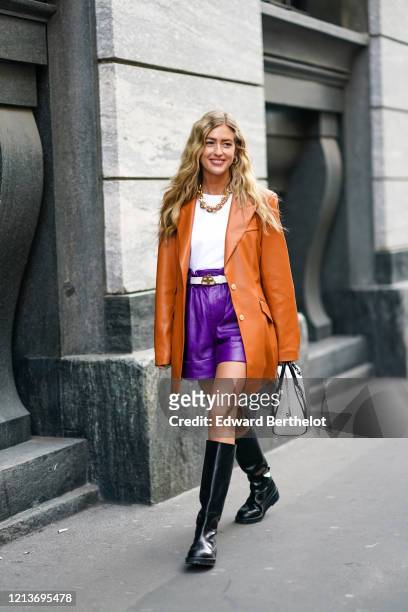 Emili Sindlev wears earrings, a necklace, a white top, a Balenciaga white belt, a tan-color leather long jacket, purple leather shorts, black...