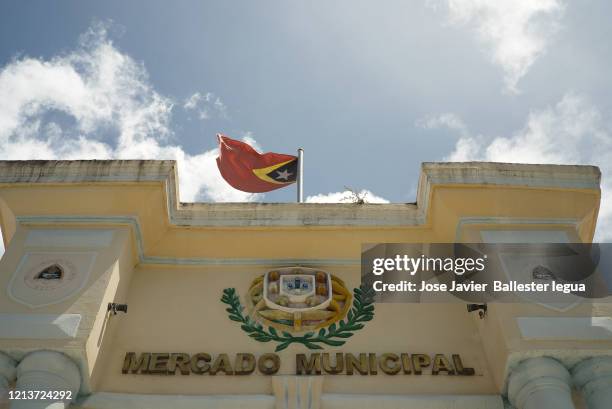 close-up of the facade of the baucau municipal market, timor leste (east timor, east timor) with a flag of timor waving .convention center. march 2020.shield - timor oriental stock pictures, royalty-free photos & images