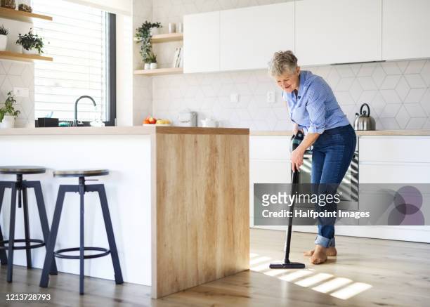 a senior woman with vacuum cleaner indoors at home, cleaning kitchen. - vacuum cleaner woman stockfoto's en -beelden