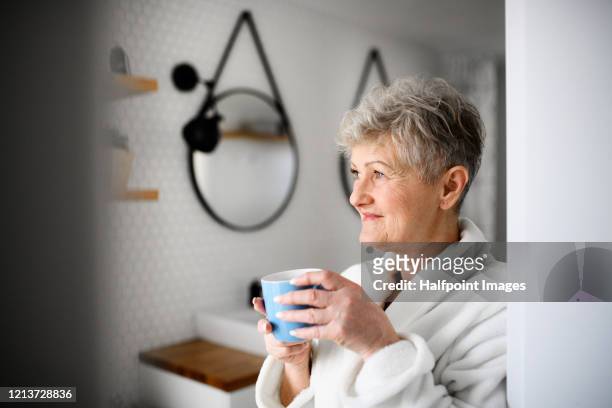 an active senior woman with bathrobe in bathroom, holding cup of coffee. - senioren in bad stock-fotos und bilder