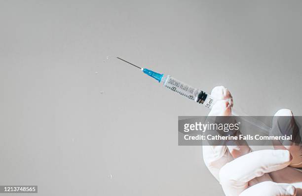 gloved hand holding a syringe - shot stockfoto's en -beelden