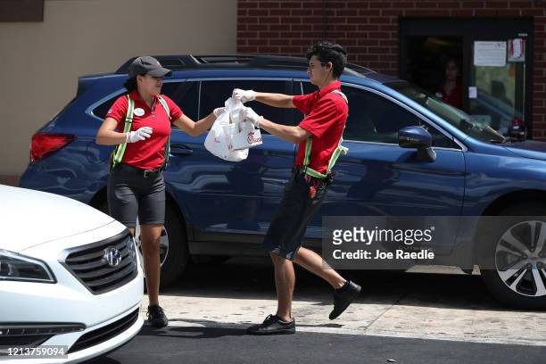 Workers at a Chick-fil-A deliver meals to customers in their vehicles at the drive-up window after the restaurant closed its indoor seating in an...