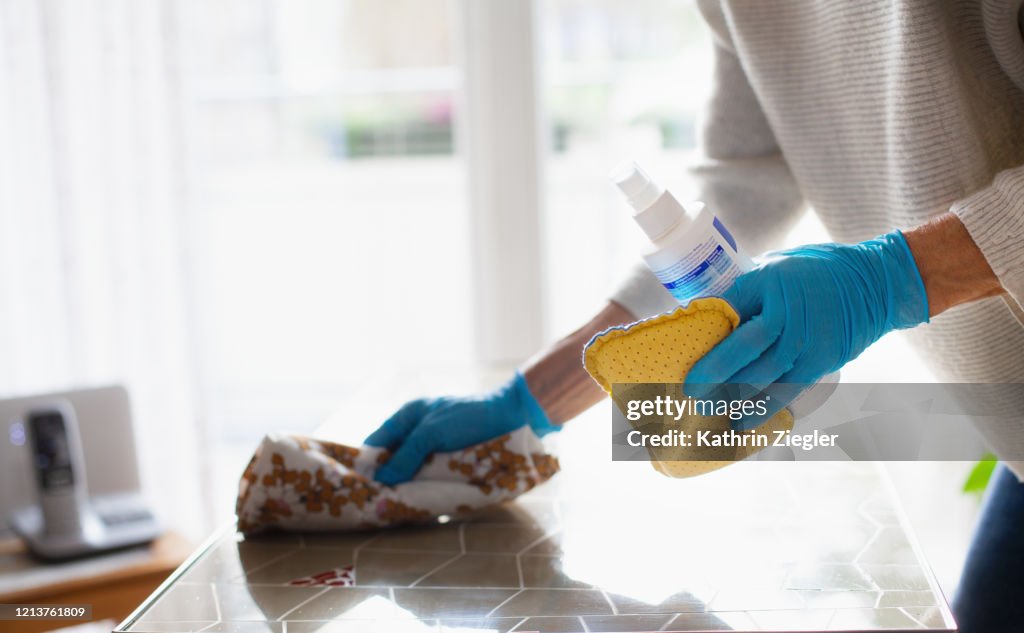 Woman cleaning table with disinfectant spray, close-up of hands in protective gloves