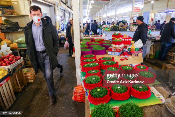 Man wears a mask and passes by wheatgrass in "8th km bazar" in on March 20, 2020 in Baku, Azerbaijan. Nowruz is among the most ancient and popular...