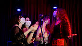 Happy young girls singing karaoke together in night club with protective face mask