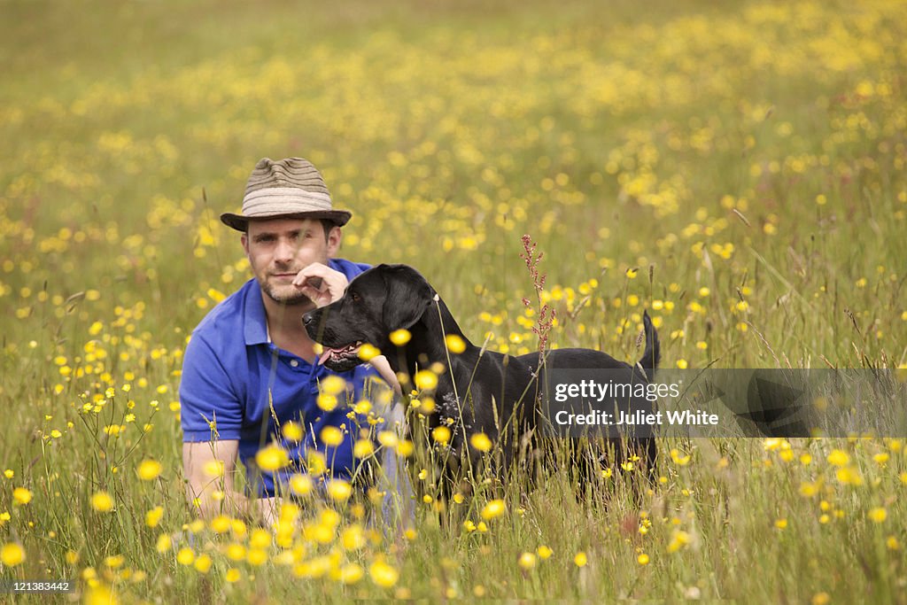 Man in Buttercup Field with Black Labrador Dog