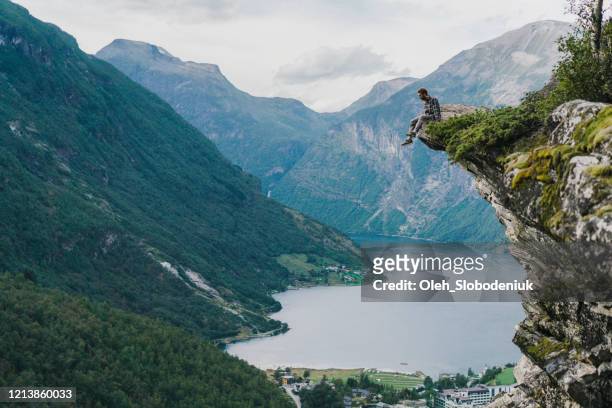 man sitting on rock near geirangerfjord in norway - cliff side stock pictures, royalty-free photos & images