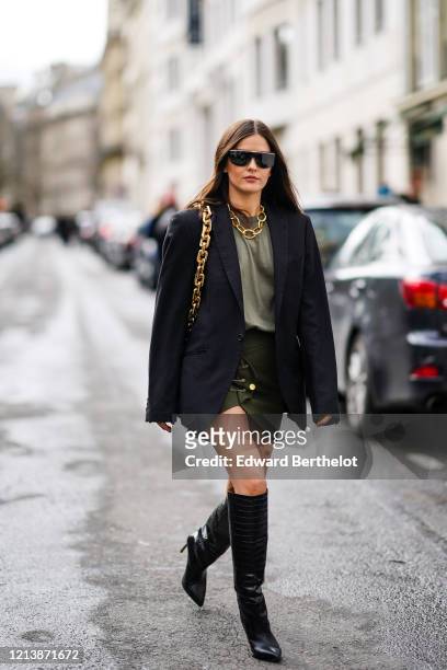Paola Alberdi wears sunglasses, a golden chain necklace, a bag with a golden chain strap, a black oversized blazer jacket, a khaki t-shirt, a green...