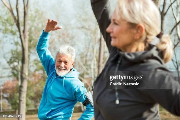 senior couple exercising in park stretching - gymnastics stock pictures, royalty-free photos & images