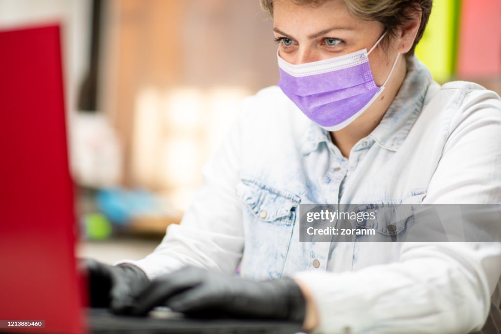 Middle aged woman working on laptop with mask on