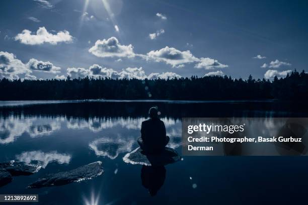 man sitting on a rock on the lake at night - wilderness area stockfoto's en -beelden