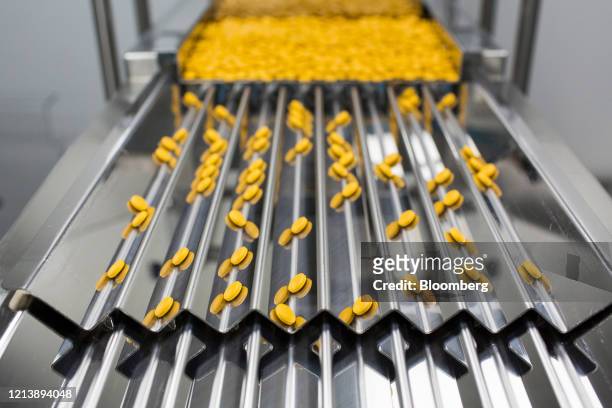 Finished tablets cascade down the channels of a packaging machine during the manufacture of the Favipiravir antiviral medicine, a joint venture...