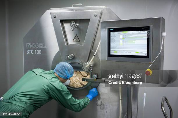 Worker wearing personal protective equipment monitors tablets in the drum of a tablet coating machine during the manufacture of the Favipiravir...