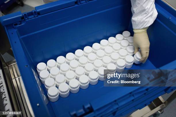 Worker wearing personal protective equipment sorts sealed containers of tablets from a packaging machine during the manufacture of the Favipiravir...