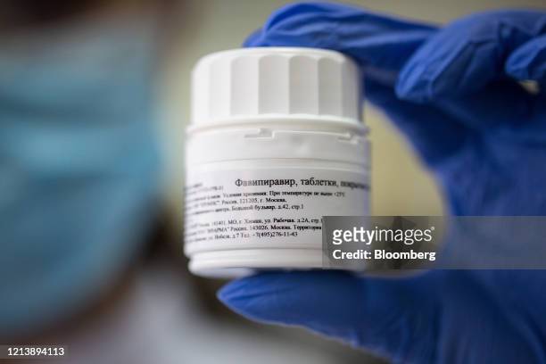 Worker wearing personal protective equipment holds a finished and sealed container of tablets in this arranged photo during the manufacture of the...