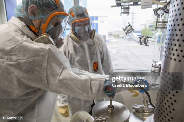 Workers dressed in personal protective equipment , including full face respirators, inspect a chemical reactor machine during the manufacture of the...