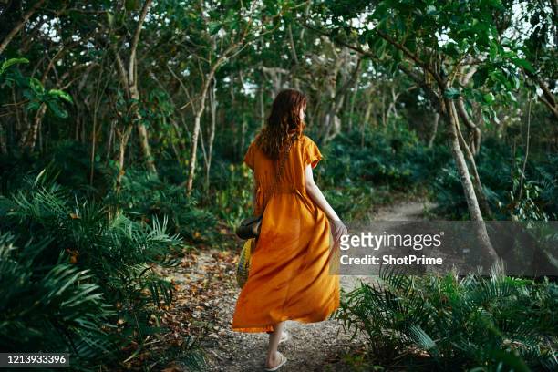 a woman in an orange dress is walking along a trail in a rainforest. - beach green stock-fotos und bilder