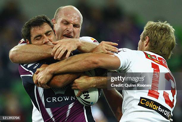 Cameron Smith of the Storm is tackled by Michael Weyman and Matt Prior of the Dragons during the round 24 NRL match between the Melbourne Storm and...