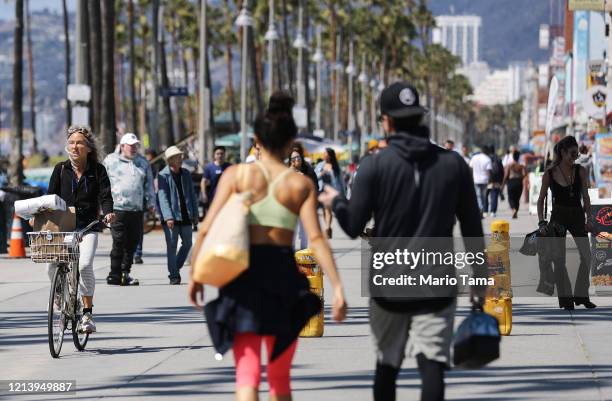 People walk along the Venice Beach boardwalk on March 21, 2020 in Venice, California. California Governor Gavin Newsom issued a ‘stay at home’ order...