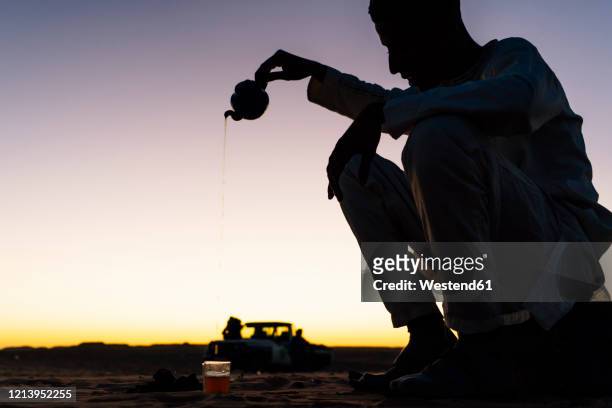 silhouette of man preparing tea in sahara desert, tindouf, algeria - algeria stockfoto's en -beelden