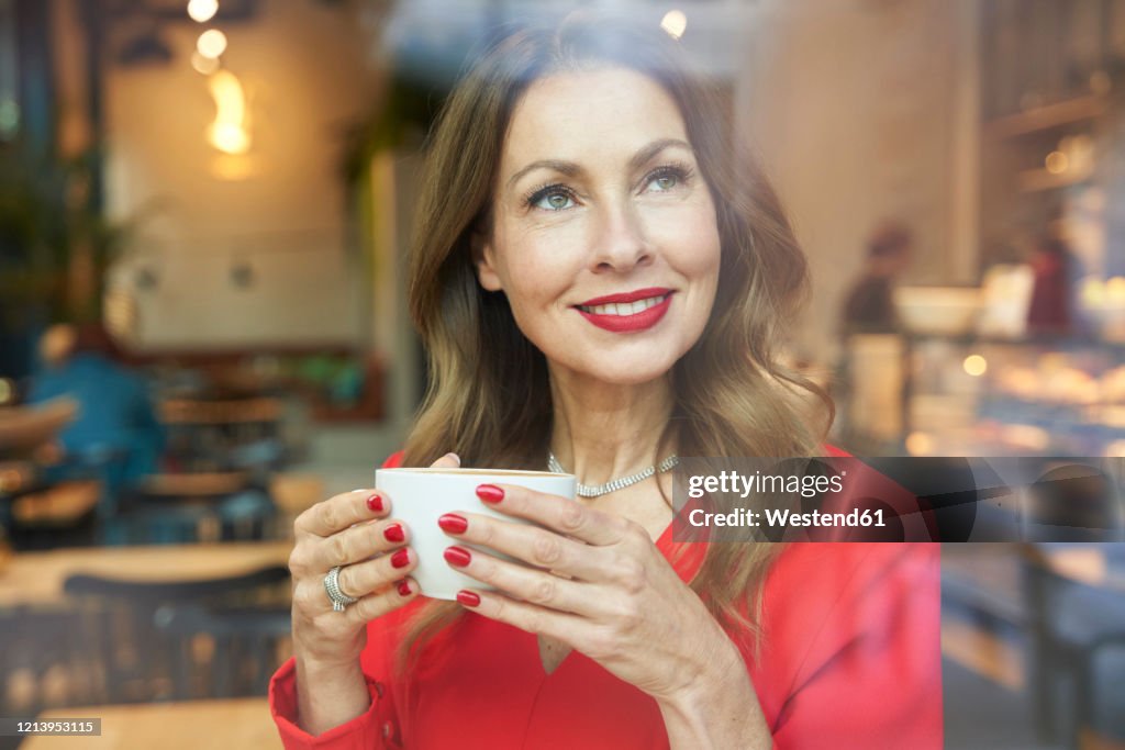 Portrait of mature woman with cup of coffee behind windowpane