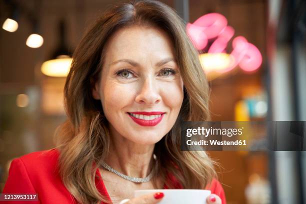 portrait of smiling mature woman with cup of coffee in a cafe - 赤の口紅 ストックフォトと画像