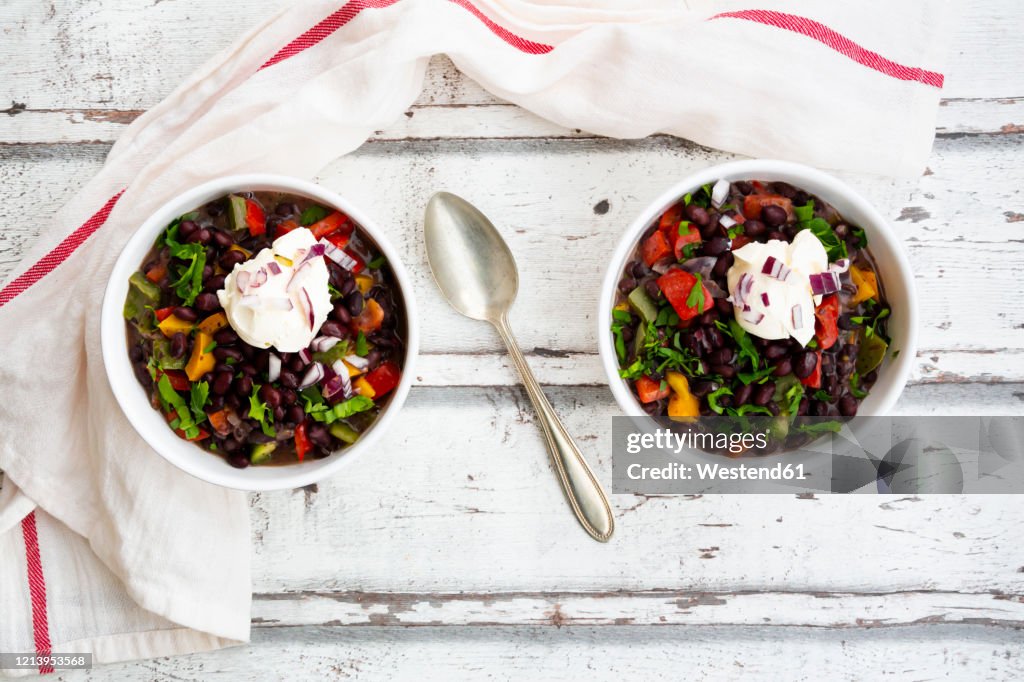 Two bowls of black bean soup withbell pepper, cilantro, sour cream and red onions