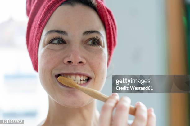 portrait of woman with head wrapped in a towel brushing heer teeth with wooden toothbrush - zahnpflege stock-fotos und bilder