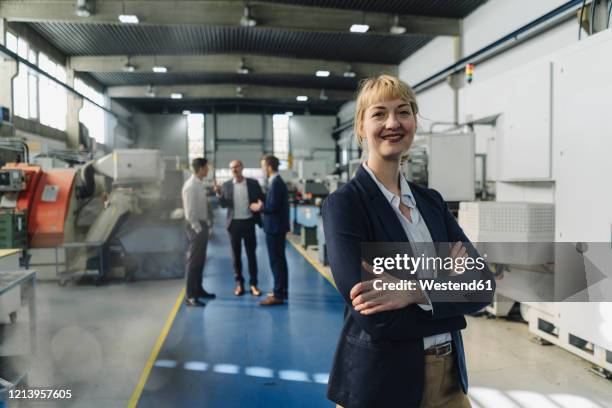 portrait of a confident businesswoman in a factory with colleagues in backgound - cosmetics industry stock pictures, royalty-free photos & images