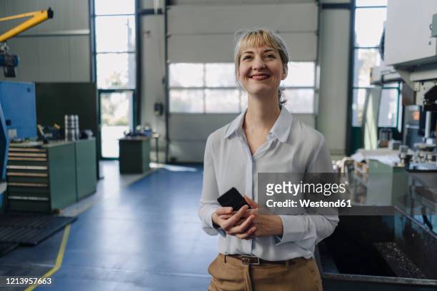 portrait of a smiling businesswoman with cell phone in a factory - einzelne frau über 30 stock-fotos und bilder